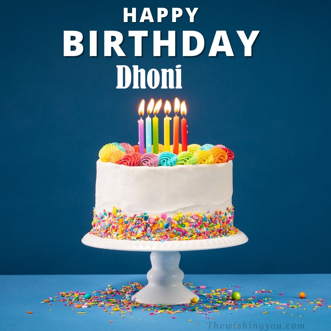 Happy birthday Dhoni written on image White cake keep on White stand and burning candles Sky background
