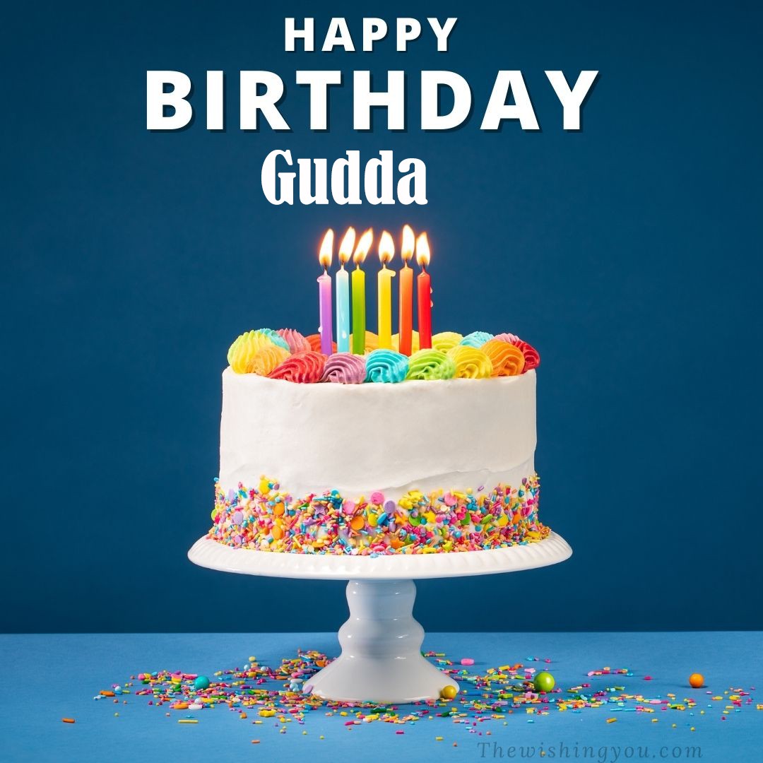 Happy birthday Gudda written on image White cake keep on White stand and burning candles Sky background